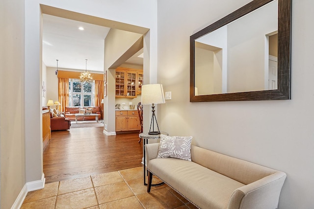 corridor with light tile patterned flooring, a notable chandelier, and baseboards