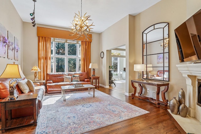 living area featuring a notable chandelier, baseboards, a fireplace with flush hearth, and wood finished floors