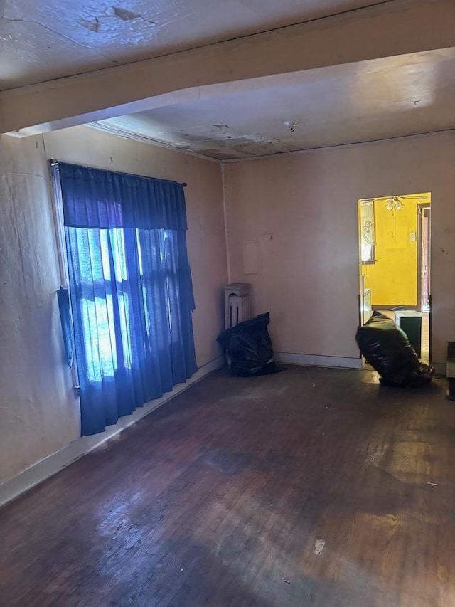 unfurnished room featuring baseboards, wood finished floors, and a wood stove