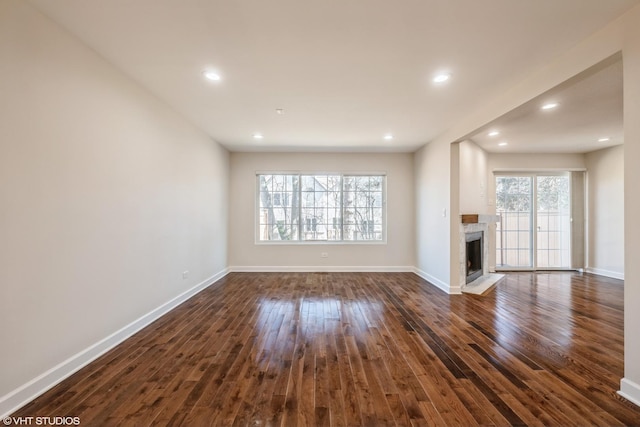 unfurnished living room with recessed lighting, baseboards, dark wood-type flooring, and a fireplace with flush hearth