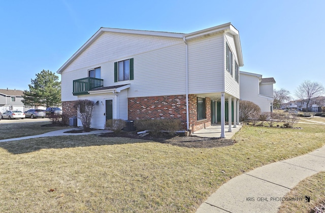 view of side of property with brick siding, a lawn, central AC, and a balcony