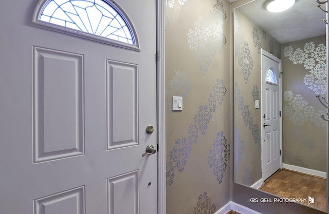 foyer featuring wallpapered walls, wood finished floors, and baseboards