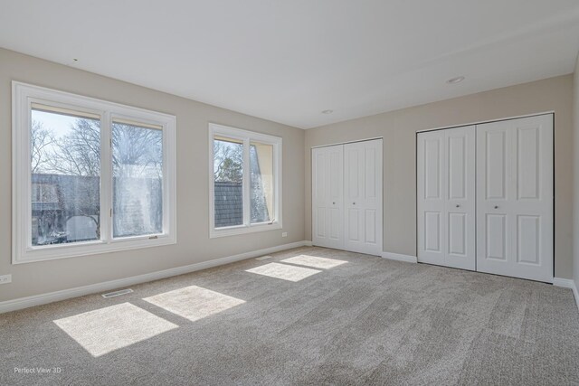 unfurnished bedroom with baseboards, visible vents, multiple closets, and carpet floors