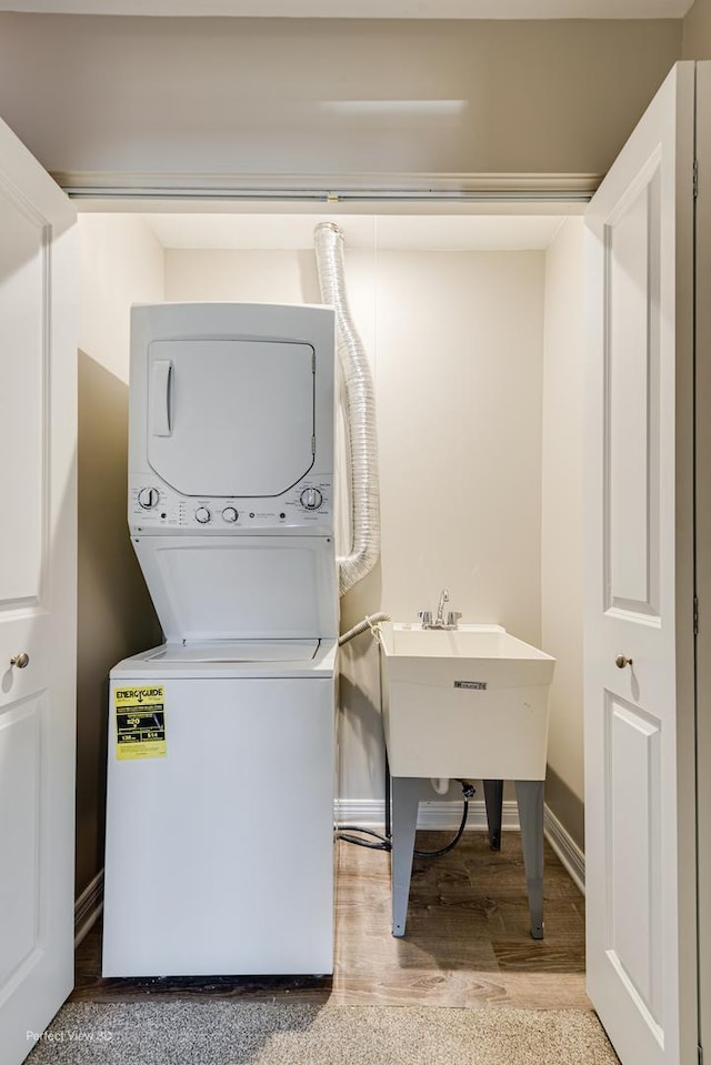 clothes washing area with light wood finished floors, stacked washer / dryer, and baseboards