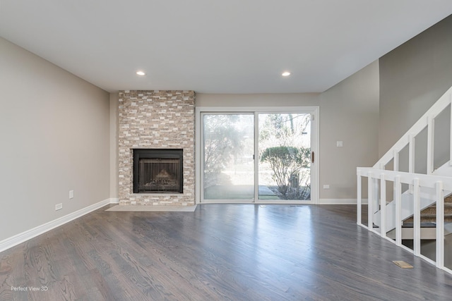 unfurnished living room with stairway, a large fireplace, baseboards, and wood finished floors