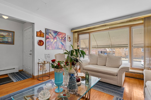 living area with a baseboard heating unit, wood-type flooring, a wealth of natural light, and ornamental molding