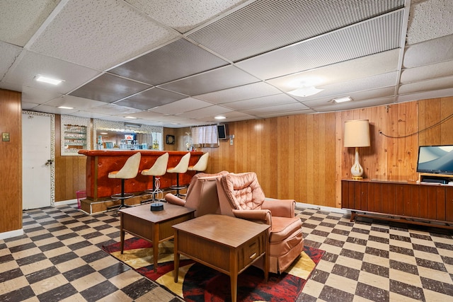 living area featuring tile patterned floors, a paneled ceiling, wood walls, and a dry bar