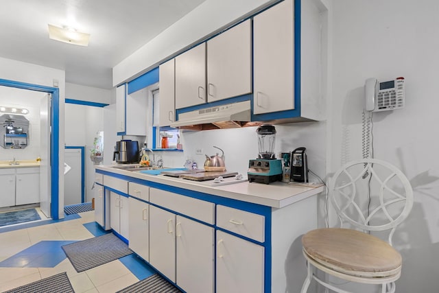 kitchen featuring light tile patterned floors, a sink, light countertops, under cabinet range hood, and white cooktop