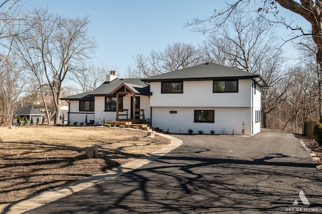 tri-level home with aphalt driveway, brick siding, a chimney, and a shingled roof