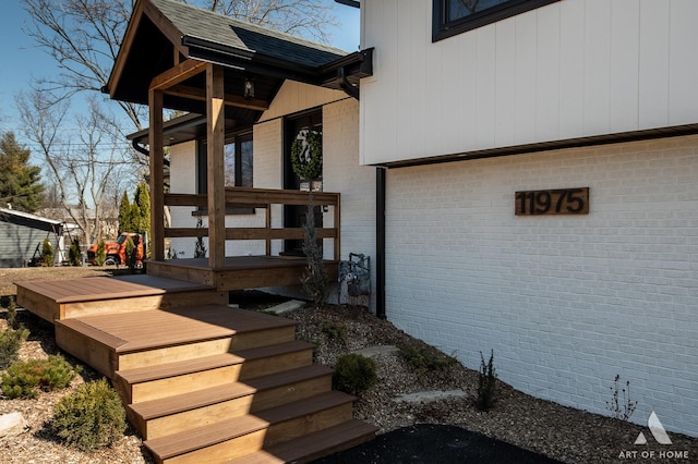 view of exterior entry with brick siding and roof with shingles