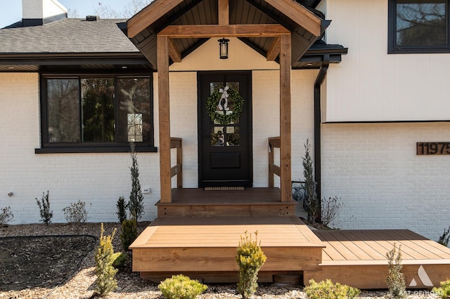 doorway to property with brick siding and a shingled roof