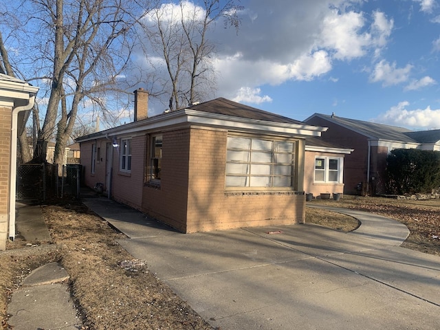 view of home's exterior featuring brick siding, driveway, a chimney, and a garage