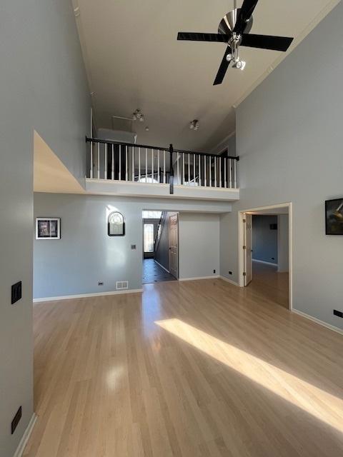 unfurnished living room featuring a towering ceiling, visible vents, wood finished floors, and a ceiling fan