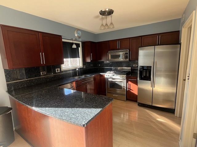 kitchen with a sink, tasteful backsplash, dark stone counters, appliances with stainless steel finishes, and a peninsula