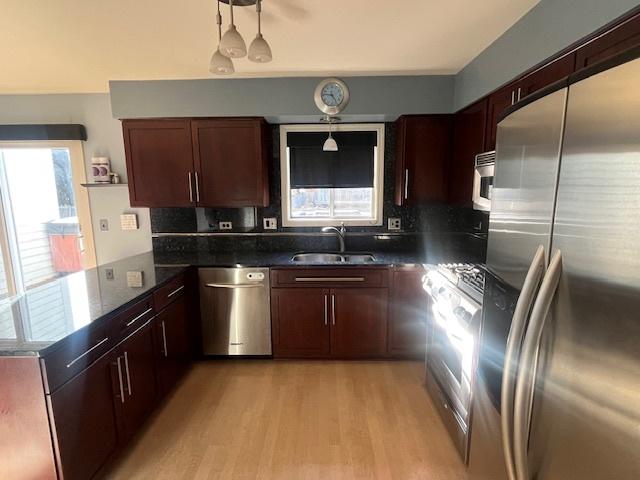 kitchen featuring a peninsula, a sink, stainless steel appliances, light wood-type flooring, and backsplash