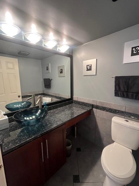 half bath featuring a wainscoted wall, toilet, tile walls, tile patterned flooring, and vanity