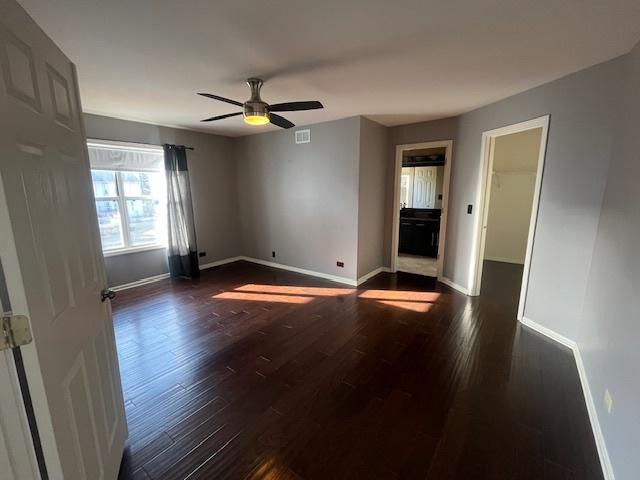 spare room with dark wood-style floors, visible vents, ceiling fan, and baseboards