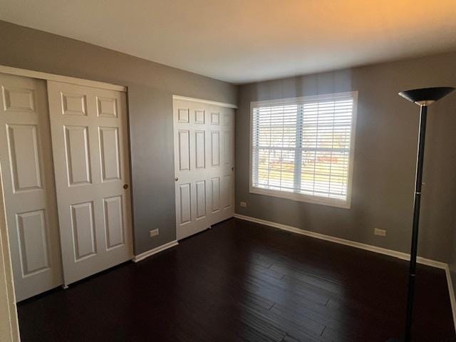 unfurnished bedroom with two closets, baseboards, and dark wood-style flooring