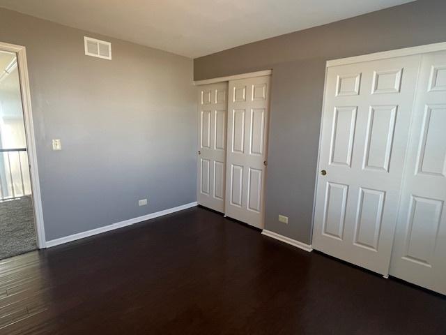 unfurnished bedroom featuring dark wood finished floors, visible vents, two closets, and baseboards