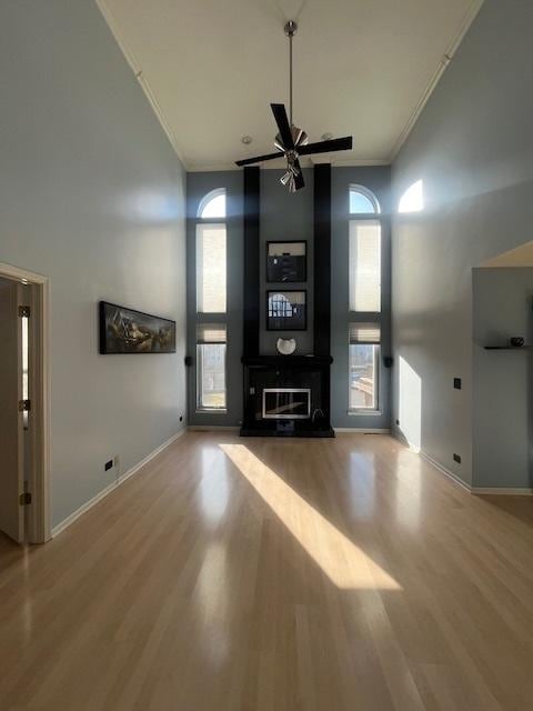 unfurnished living room with plenty of natural light, crown molding, a towering ceiling, and wood finished floors