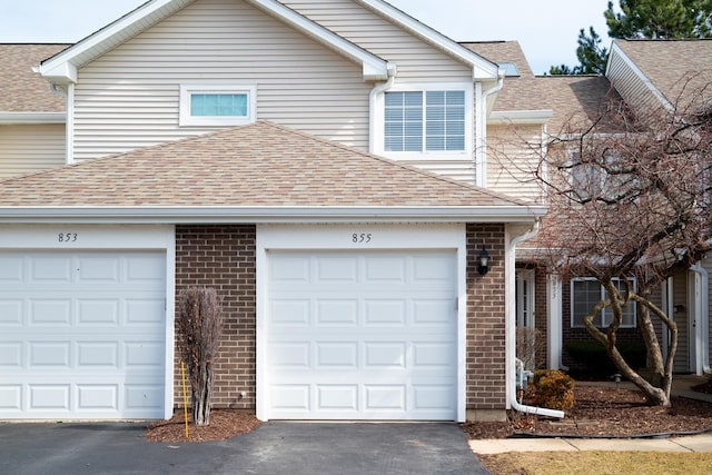 view of front of house featuring a garage, brick siding, roof with shingles, and driveway