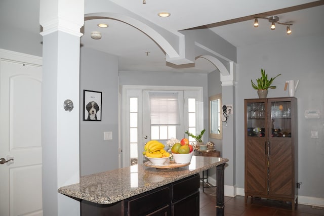 kitchen featuring light stone counters, dark tile patterned floors, baseboards, and decorative columns