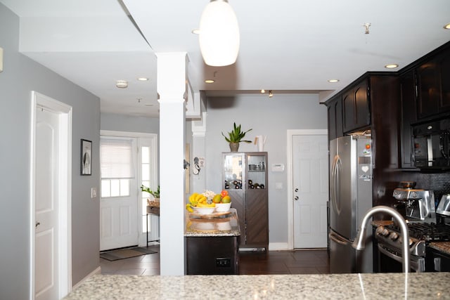 kitchen featuring light stone countertops, dark brown cabinetry, appliances with stainless steel finishes, ornate columns, and dark tile patterned flooring