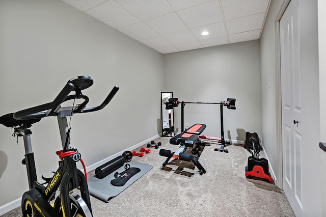 exercise room featuring a paneled ceiling, baseboards, and carpet