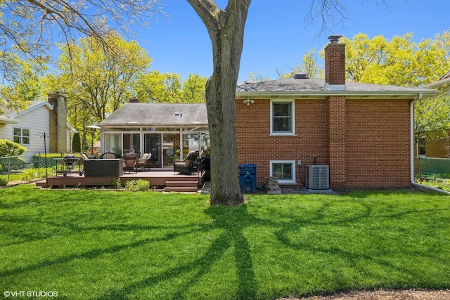 rear view of house with brick siding, a lawn, a chimney, a deck, and a sunroom