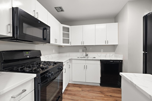 kitchen featuring light stone counters, visible vents, a sink, black appliances, and light wood-style floors