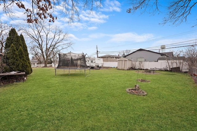 view of yard featuring an outbuilding, a fenced backyard, a storage shed, and a trampoline