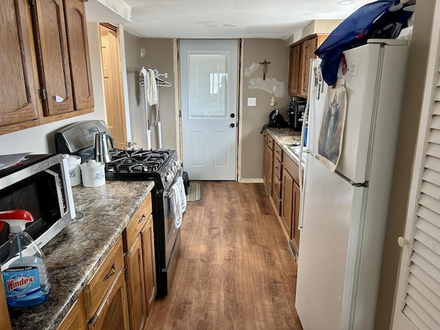 kitchen featuring wood finished floors, dark stone counters, brown cabinetry, and stainless steel appliances