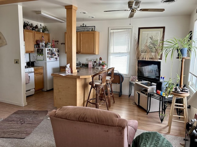 kitchen featuring white appliances, ornate columns, a peninsula, a kitchen breakfast bar, and open floor plan