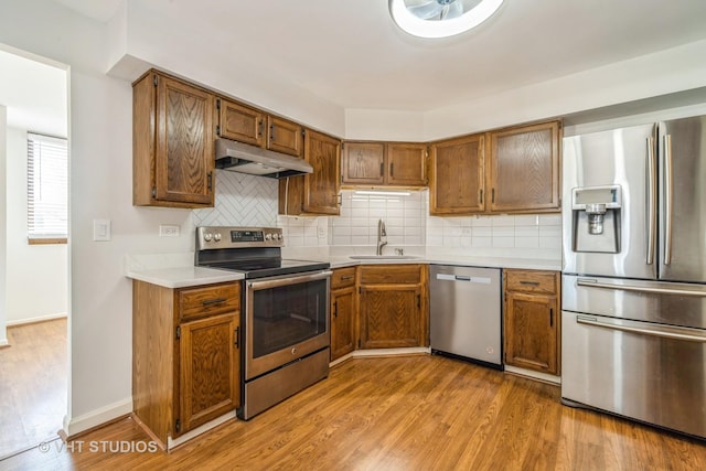 kitchen with wood finished floors, a sink, light countertops, under cabinet range hood, and appliances with stainless steel finishes