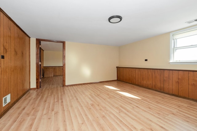 empty room featuring wooden walls, visible vents, and light wood finished floors