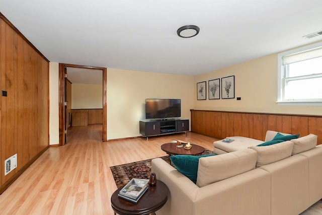 living area with light wood-style floors, visible vents, and wood walls