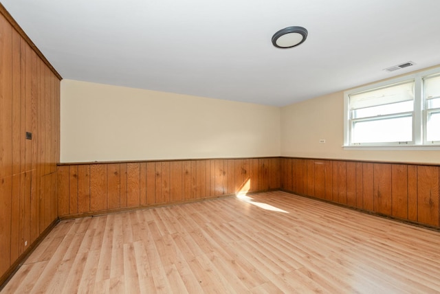 spare room with visible vents, a wainscoted wall, wood walls, and light wood-style flooring