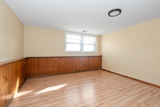 empty room featuring light wood-type flooring, visible vents, wood walls, and wainscoting