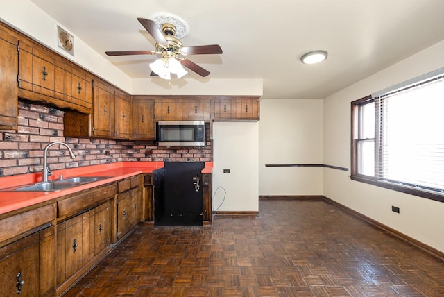 kitchen featuring a sink, stainless steel microwave, brown cabinetry, baseboards, and ceiling fan