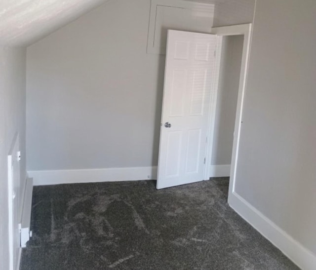 unfurnished bedroom featuring baseboards, lofted ceiling, and dark colored carpet