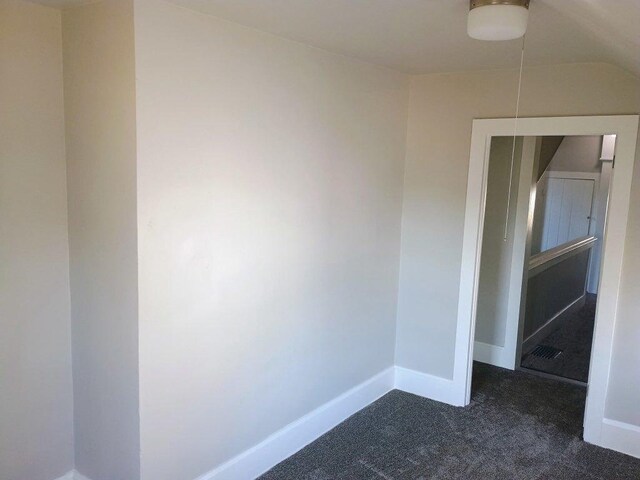 unfurnished room featuring dark colored carpet and baseboards