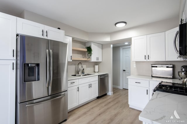 kitchen with light stone counters, light wood finished floors, a sink, white cabinets, and appliances with stainless steel finishes