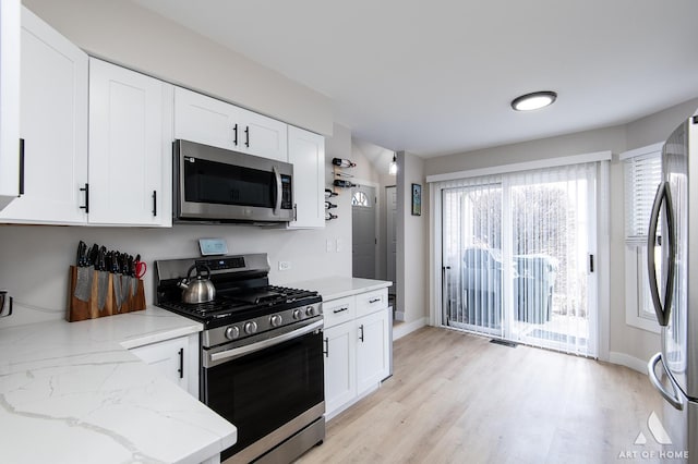 kitchen with white cabinets, stainless steel appliances, light wood-type flooring, and light stone countertops