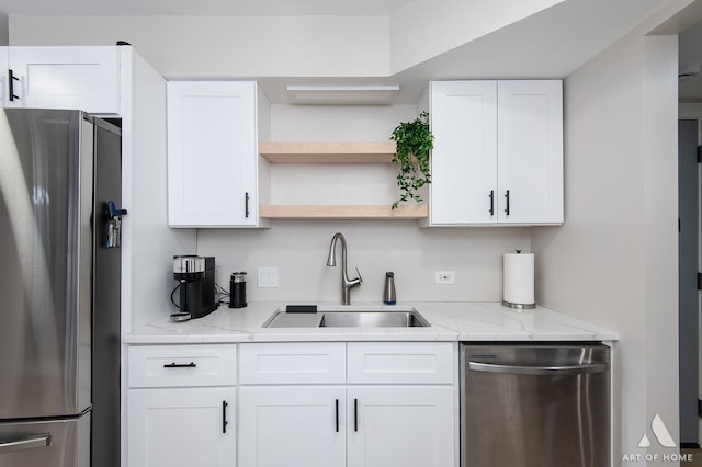 kitchen with a sink, stainless steel appliances, light stone countertops, and white cabinets