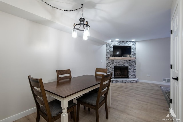 dining room featuring baseboards, a fireplace, visible vents, and light wood-type flooring