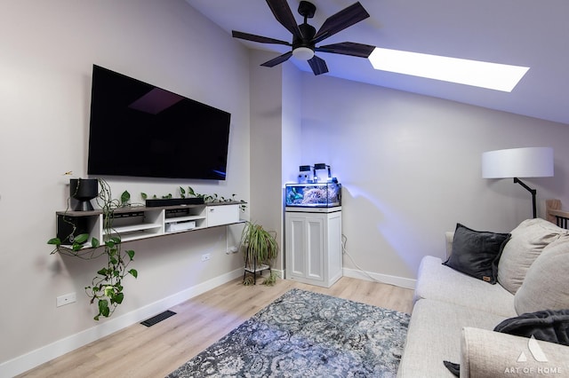 living area with visible vents, lofted ceiling with skylight, a ceiling fan, wood finished floors, and baseboards