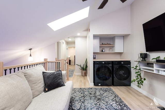 living area featuring vaulted ceiling with skylight, baseboards, light wood-type flooring, and washer and clothes dryer