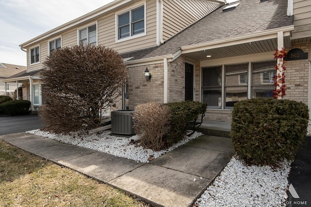 view of front of home featuring a porch, central AC unit, brick siding, and a shingled roof