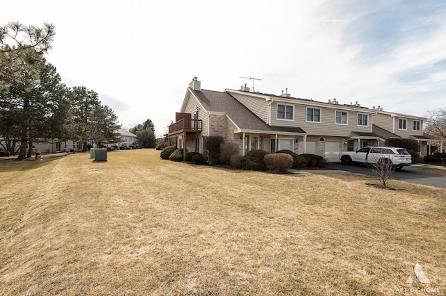 view of front of property featuring a front lawn, aphalt driveway, a garage, a balcony, and a chimney