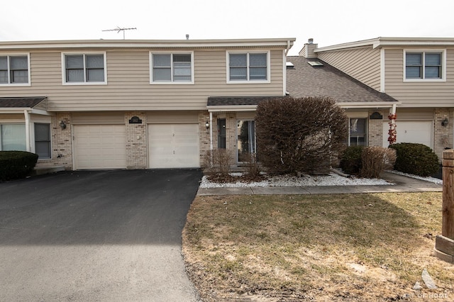 multi unit property featuring brick siding, driveway, an attached garage, and a shingled roof